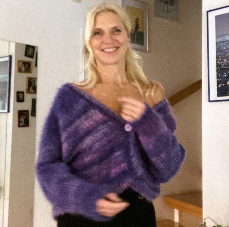 May include: A purple and pink fluffy cardigan with a single button closure. The cardigan is made of a soft, fluffy material and has a relaxed fit.