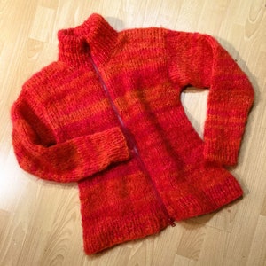 Pode incluir: Um cardigan de malha listrado vermelho e laranja com fecho de zíper.