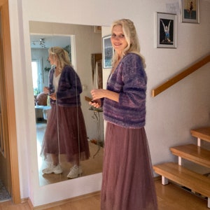 May include: A woman wearing a purple and pink striped cardigan with a long, dusty rose tulle skirt and white trainers.