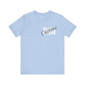Könnte beinhalten: Ein hellblaues T-Shirt mit dem Text "Custom DM" in grauer und weißer Schrift.