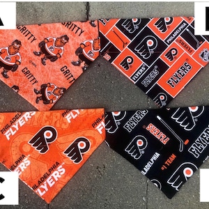May include: Four different dog bandanas featuring the Philadelphia Flyers logo. The bandanas are in orange, black, and white with the Flyers logo and text. The bandanas are in a triangular shape.