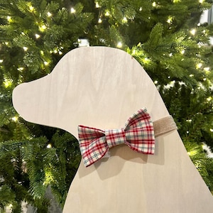 May include: A white wooden dog silhouette with a red and white plaid bow tie. The bow tie is tied around the dog's neck with a tan ribbon.