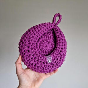 May include: A purple crocheted hanging basket with a loop handle. The basket has a small tag that says "Hand Made".
