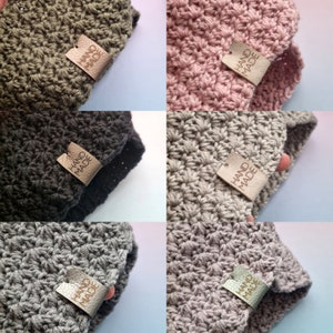 May include: Four crocheted hats in different colours: green, pink, grey, and black. Each hat has a brown leather tag that says "HAND MADE".