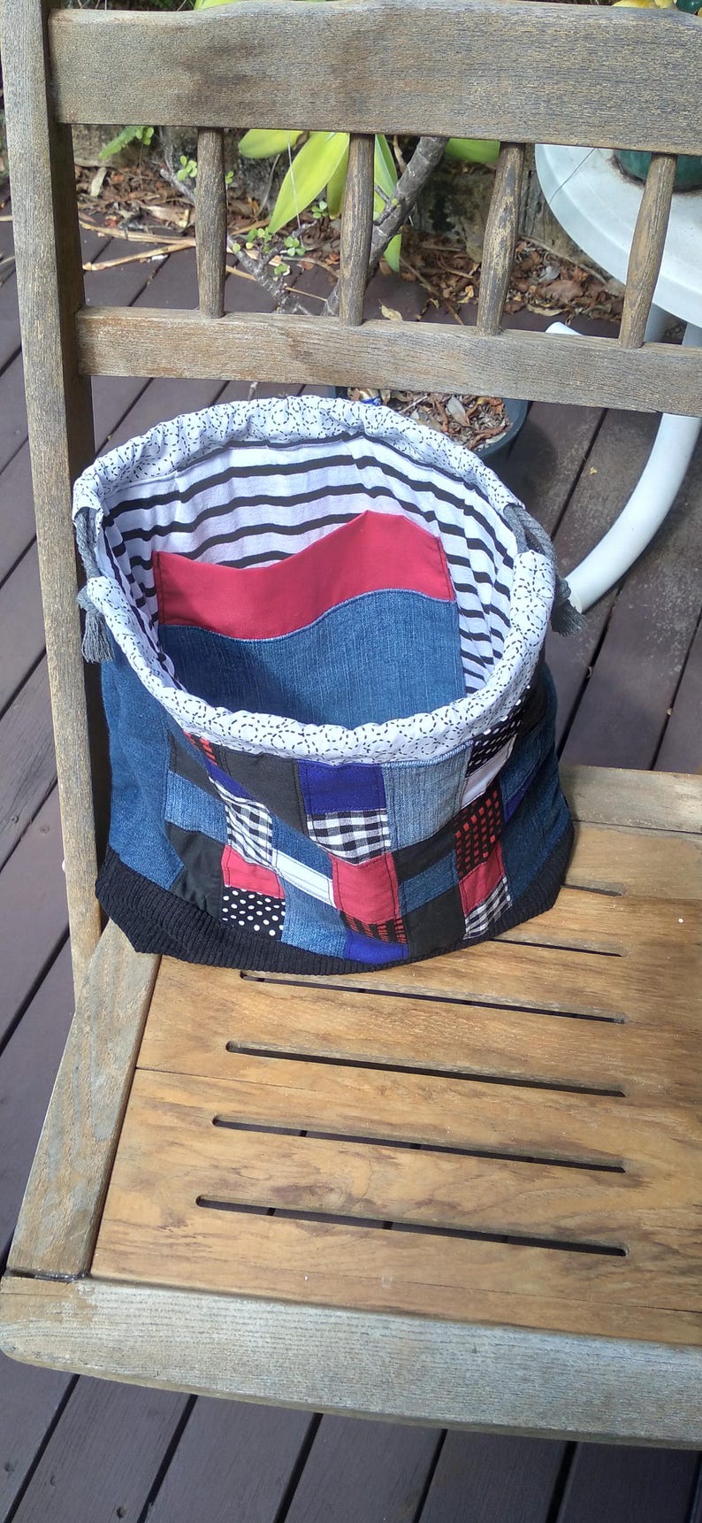 May include: A handmade patchwork tote bag with a denim exterior. The bag features a variety of fabric patches in blue, red, black, and white. The interior lining is striped, and the top edge is trimmed with white lace.