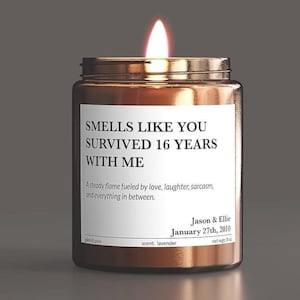 May include: A lit candle in a brown glass jar with a white label reading: SMELLS LIKE YOU SURVIVED 16 YEARS WITH ME, A steady flame fueled by love, laughter, sarcasm, and everything in between. Jason & Ellie January 27th, 2010, net wgt: 8 oz.