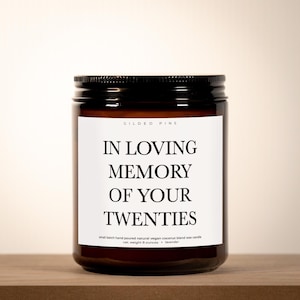 A brown glass jar with a black lid, featuring a white label with black text that reads "IN LOVING MEMORY OF YOUR TWENTIES".