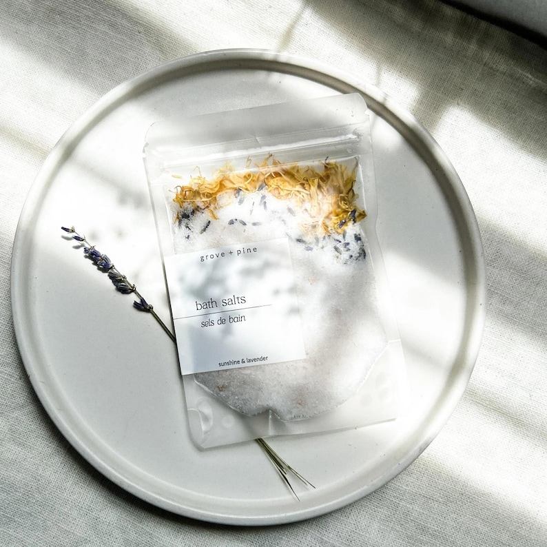 A white plate with a package of bath salt on it, placed on a white surface with sunlight shining on it.