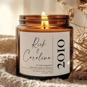 May include: A lit candle in an amber glass jar with a white label featuring the names Rick & Carolina, the year 2010, and the text 16 years together! From first spark to forever. The label also lists scent: peace + clarity + breath and net weight: 8 oz.
