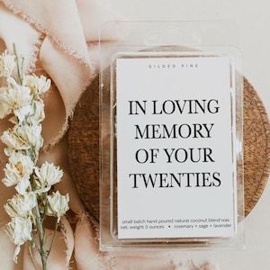 a clear plastic container with a label that reads "In Loving Memory of Your Twenties" and contains a small batch hand poured natural coconut blend wax, net weight of 3 ounces, rosemary, and lavender.