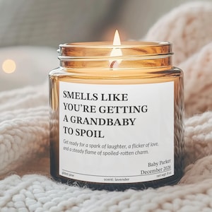 A lit candle in a glass jar sits on a white blanket, with a blurred background of a cozy living space.