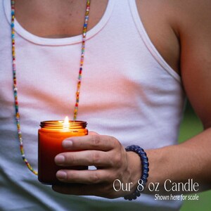 A person is holding a lit candle in their hand, wearing a white tank top and a colorful beaded necklace.