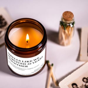 a brown candle with a lit flame, a small glass jar with a cork lid, and some photographs arranged on a white surface.