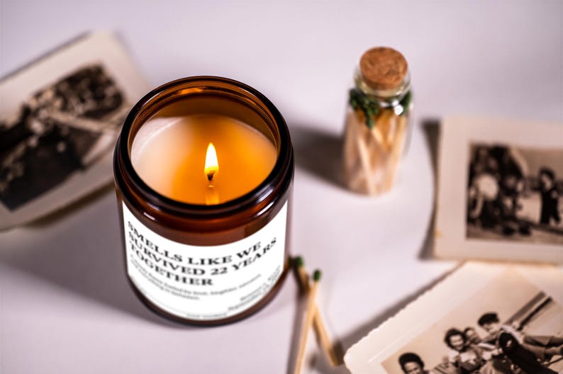 a brown candle with a lit flame, a small glass jar with a cork lid, and some photographs arranged on a white surface.