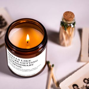 a brown candle with a lit flame, a small glass jar with a cork lid, and some photographs arranged on a white surface.