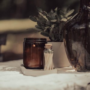 a brown glass jar, a white vase with a plant, and a brown glass bottle, all placed on a white surface.