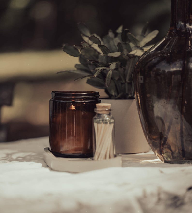 a brown glass jar, a white vase with a plant, and a brown glass bottle, all placed on a white surface.