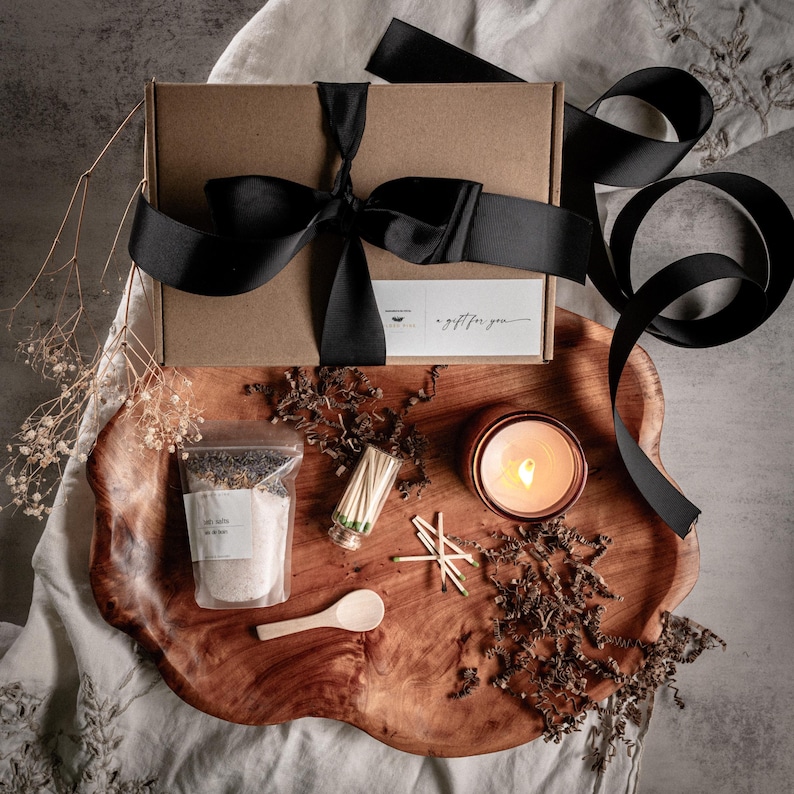 a wooden tray with various items arranged on it, including a candle, a bag of salt, a wooden spoon, and some dried flowers.