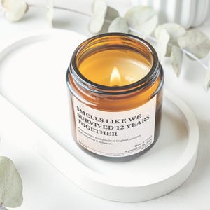 A brown glass jar with a white label sits on a white tray, surrounded by eucalyptus leaves and other greenery.