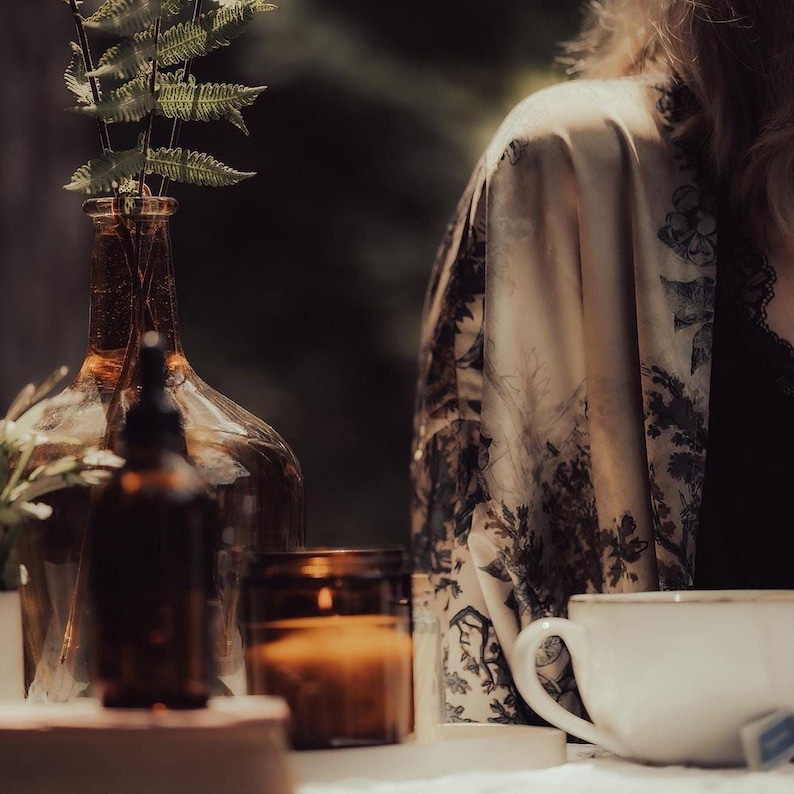 a table with various objects, including a vase with ferns, a candle, a white mug, and a glass bottle.