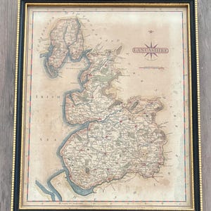 May include: A framed vintage-style map of Lancashire, England, featuring detailed topography, town names, and a compass rose. The map is presented in a black frame with gold trim, displaying the text LANCASHIRE in a central box with a scale bar.