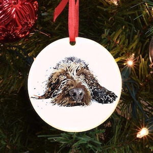 May include: A white ceramic Christmas bauble featuring a watercolour illustration of a brown and white dog with its head resting on its paws. The dog has a brown nose and brown eyes.