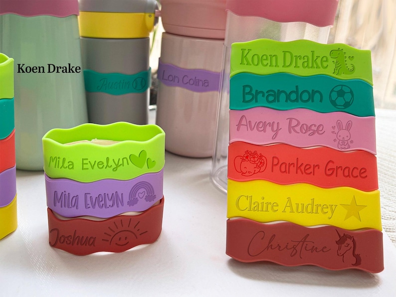 May include: A set of colorful, wavy silicone labels with names and small icons. The labels are green, purple, red, yellow, and pink. The names on the labels are Koen Drake, Mila Evelyn, Joshua, Brandon, Avery Rose, Parker Grace, Claire Audrey, and Christine.