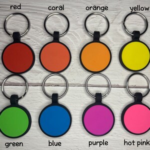 May include: A collection of eight colorful keychains. Each keychain features a round, colored disc with a black border and a silver keyring. Colors include red, coral, orange, yellow, green, blue, purple, and hot pink. The colors are labeled.