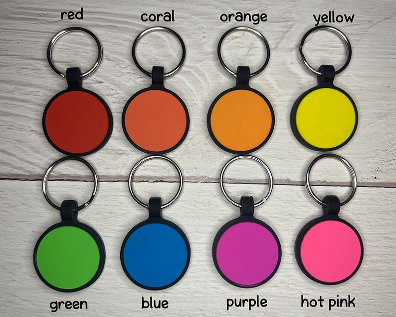 May include: A collection of eight colorful keychains. Each keychain features a round, colored disc with a black border and a silver keyring. Colors include red, coral, orange, yellow, green, blue, purple, and hot pink. The colors are labeled.