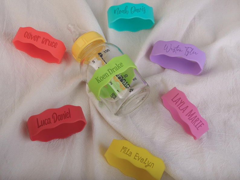 May include: A set of ten colorful silicone bottle labels with names printed on them. The labels are in various colors, including red, pink, purple, yellow, and green. The labels are designed to be used on baby bottles.