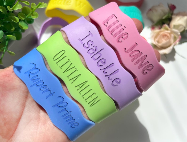 May include: Five colorful silicone bracelets with wavy edges and personalized names: Rupert Prime, Olivia Allen, Isabelle, Ellie Jane.