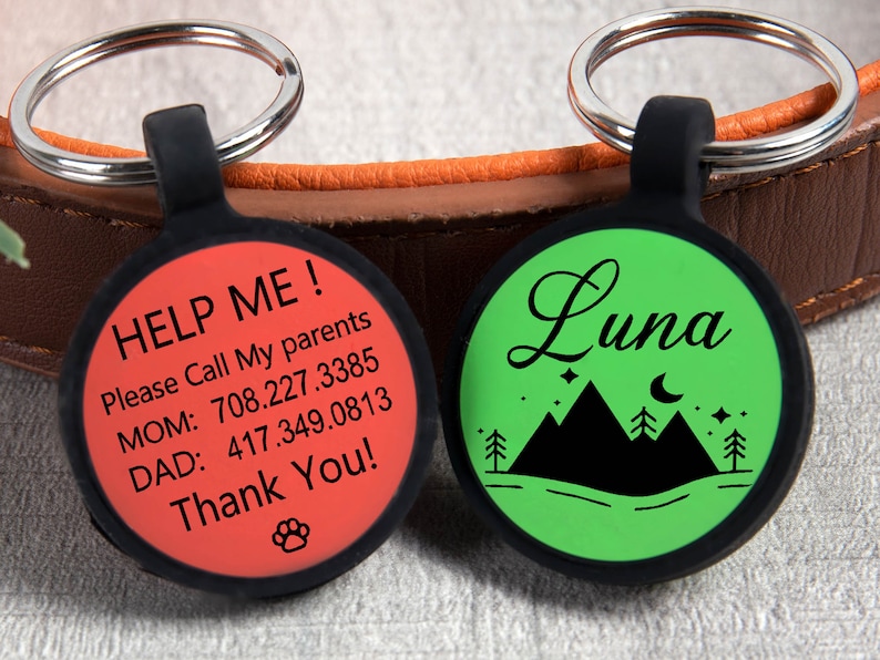 May include: Two round pet ID tags with black trim and silver rings. One tag is red with "HELP ME!" and contact information. The other is green with the name "Luna" and a mountain scene.