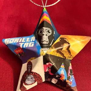 May include: A star-shaped ornament made from paper with a collage of images of monkeys wearing different costumes. The ornament has a silver string attached to the top for hanging.