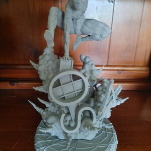 K&ouml;nnte beinhalten: Eine graue, 3D-gedruckte Figur von Spider-Man, die auf einem Sockel mit einem Spinnennetz-Design steht. Der Sockel zeigt auch ein 3D-gedrucktes Design eines Spinnennetzes und eines Symbols.