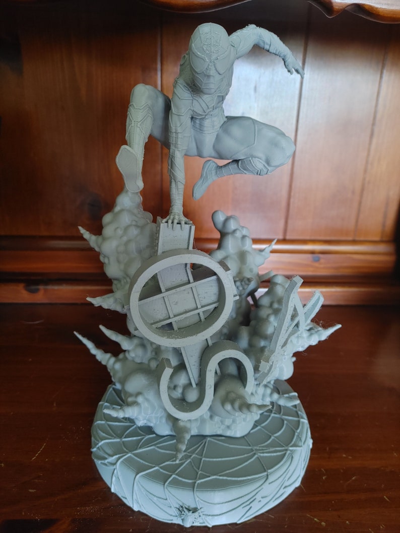 K&ouml;nnte beinhalten: Eine graue, 3D-gedruckte Figur von Spider-Man, die auf einem Sockel mit einem Spinnennetz-Design steht. Der Sockel zeigt auch ein 3D-gedrucktes Design eines Spinnennetzes und eines Symbols.