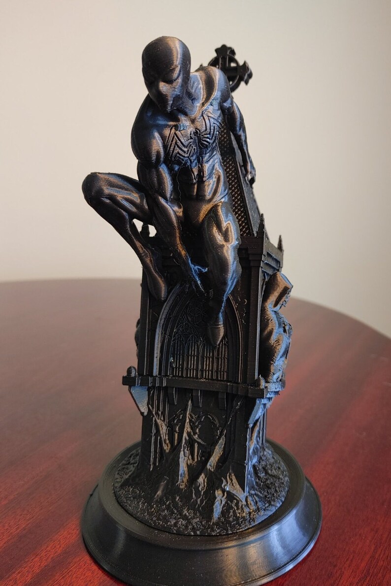K&ouml;nnte beinhalten: Schwarze 3D-gedruckte Figurine von Spider-Man, die auf einer gotischen Kathedralenstruktur thront. Die Figur ist in einer dynamischen Action-Pose dargestellt, mit einem erhobenen Bein und dem anderen Bein, das im Knie gebeugt ist. Die Kathedrale ist mit aufwendigen Schnitzereien und einem Kreuz an der Spitze verziert.