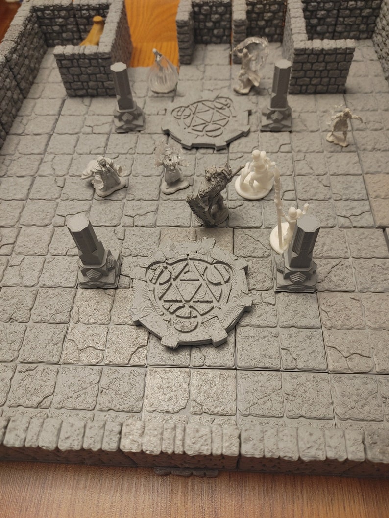 K&ouml;nnte beinhalten: Ein graues Tabletop-Spielset mit Miniaturfiguren und einer steinartigen Textur. Das Set enth&auml;lt eine runde Basis mit einem Pentagramm-Design, S&auml;ulen und Figuren verschiedener Charaktere.