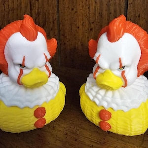Könnte beinhalten: Zwei gelbe Gummienenten mit weißen Kragen und roten Akzenten. Die Enten haben orangefarbenes Haar und weiße Gesichter mit roten, gemalten Linien. Die Enten schauen nach rechts.