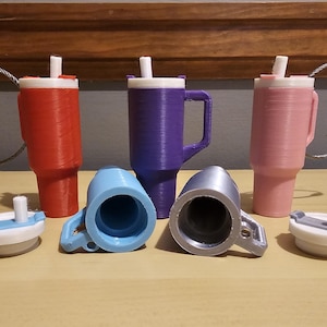 May include: Five 3D printed travel mugs with lids and keychains. The mugs are in red, purple, pink, blue, and silver.