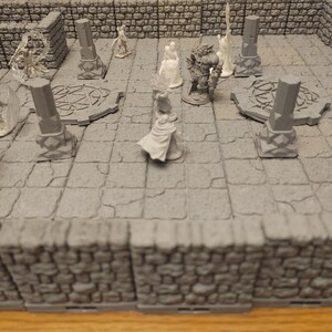 K&ouml;nnte beinhalten: Ein Miniatur-Tabletop-Spielset mit grauen Steinw&auml;nden und einem grauen Steinboden. Auf dem Boden befinden sich mehrere Miniaturfiguren, darunter ein Krieger, ein Zauberer und eine Kreatur. Die Figuren sind aus wei&szlig;em Kunststoff.