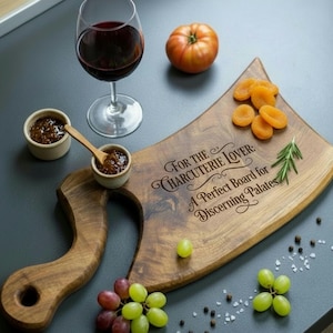 Puede incluir: Tabla de charcutería de madera con asa, grabada con texto. La imagen incluye una copa de vino tinto, pequeños cuencos de mermelada, albaricoques secos, uvas y un tomate. Una ramita de romero añade un toque fresco.