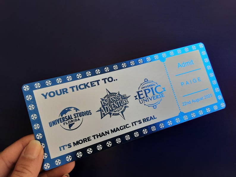 Pu&ograve; includere: Un biglietto argentato con accenti blu per l'ammissione a Universal Studios Islands of Adventure e Universal's Epic Universe. Il biglietto recita "Your Ticket To..." e "It's More Than Magic. It's Real." Il biglietto &egrave; per Paige ed &egrave; datato 22 agosto 2025.