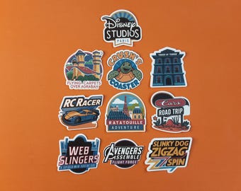 May include: A collection of colorful stickers featuring various Disney theme park attractions. Designs include "Disney Studios Paris," "Crush's Coaster," "Tower of Terror," "RC Racer," "Cars Road Trip," and more. The stickers are on an orange background.