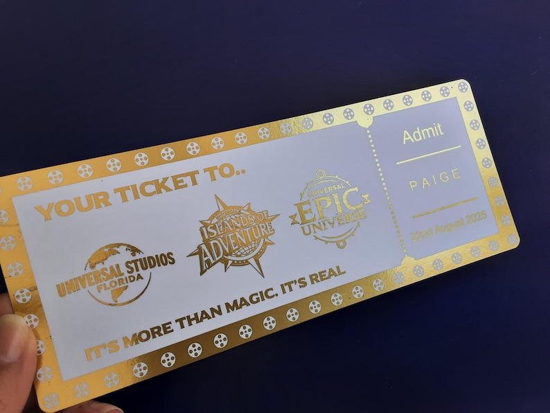 Pu&ograve; includere: Un biglietto dorato con testo bianco che recita "Your Ticket To..." e presenta i loghi di Universal Studios Florida, Islands of Adventure ed Epic Universe. Il biglietto &egrave; per Paige ed &egrave; datato 20 agosto 2005.