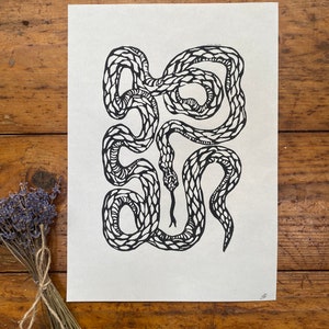 May include: Black and white line art print of a snake coiled in a circle. The snake is drawn with a detailed pattern of scales.