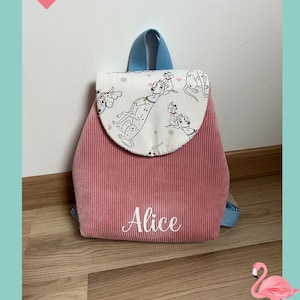 May include: A pink corduroy backpack featuring a white flap with a black and white Dalmatian dog print and small pink hearts. The name Alice is embroidered in white script on the front pocket. The backpack has light blue straps and trim.