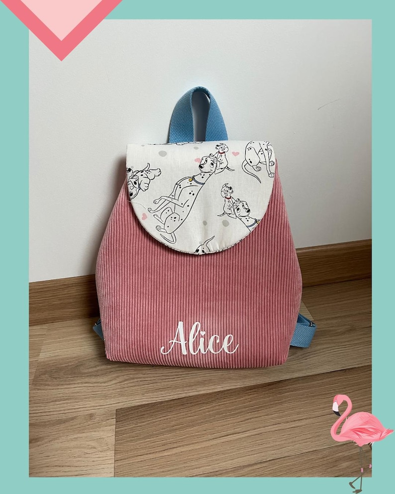 May include: A pink corduroy backpack featuring a white flap with a black and white Dalmatian dog print and small pink hearts. The name Alice is embroidered in white script on the front pocket. The backpack has light blue straps and trim.