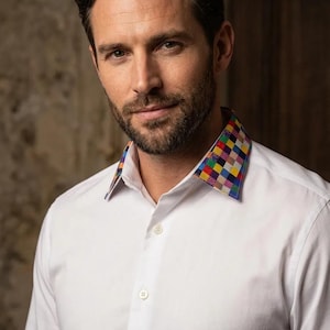 May include: A crisp white long-sleeved button-down shirt featuring a vibrant, multi-coloured checkered pattern on the inner and outer collar. The shirt has a standard point collar, a front button placket with matching white buttons, and long sleeves.