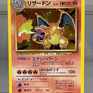 Op de afbeelding: Charizard Pokémon-verzamelkaart met gele rand. De kaart toont een gedetailleerde illustratie van Charizard, een vurige oranje draak, met Japanse tekst en symbolen. De kaart heeft level 76 en 120 HP.