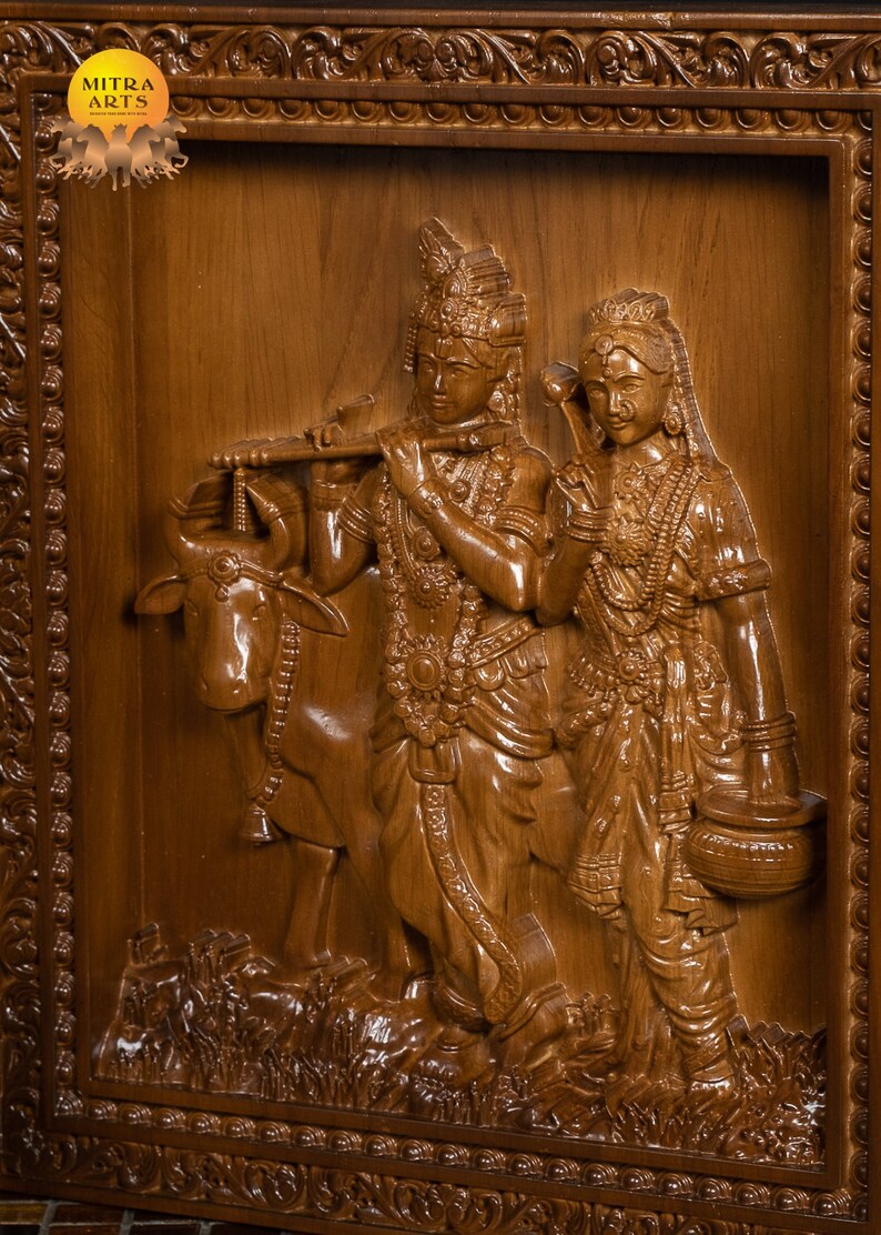 K&ouml;nnte beinhalten: Eine Holzschnitzerei, die ein Paar, m&ouml;glicherweise Radha und Krishna, mit einer Kuh zeigt. Die Schnitzerei ist detailliert und kunstvoll, die Figuren tragen aufwendige Kleidung und Schmuck. Die Schnitzerei ist in einem Holzrahmen mit verzierten Details gefasst.
